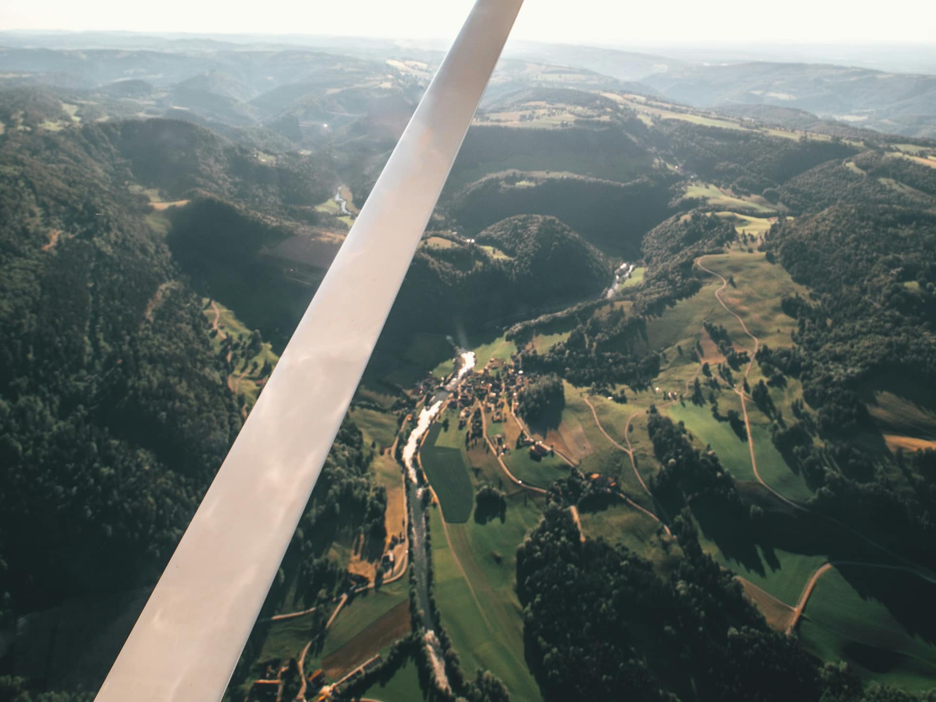 Forested hills and a green river valley seen past the wing strut of a high-wing airplane